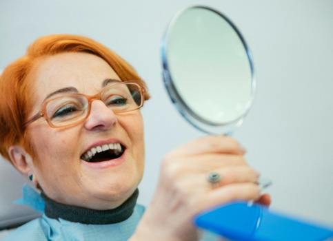 An elderly woman admiring her dentures in a hand mirror