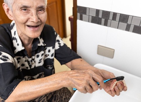 Someone cleaning dentures with a toothbrush