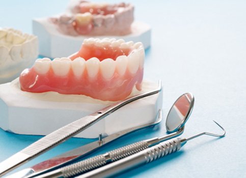 A closeup of bottom dentures next to dental tools