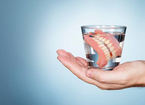 A closeup of dentures soaking in a glass