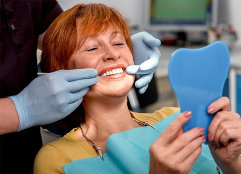 A woman admiring her new dentures in a hand mirror