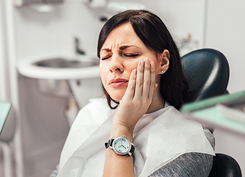 Woman in need of wisdom tooth extraction holding jaw