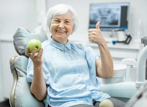 woman in dental chair giving thumbs up and holding green apple 