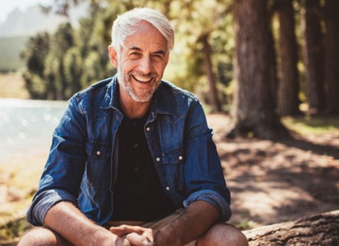 smiling man sitting on a log by a lake   