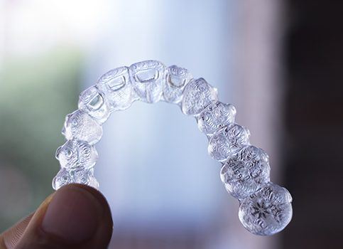Hand holding a clear Invisalign tray