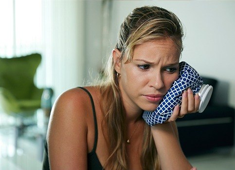 Woman holding ice pack to cheek after tooth extraction