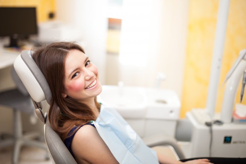 a young female sitting in the dentist’s chair and smiling while waiting to see her dental professional