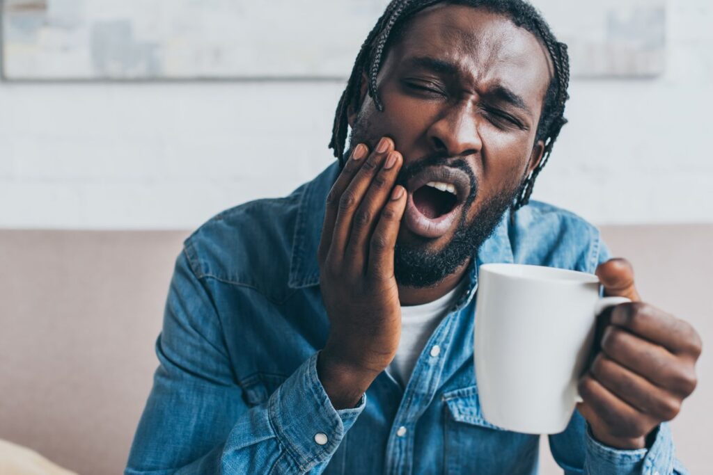 A man with a toothache holding a coffee cup