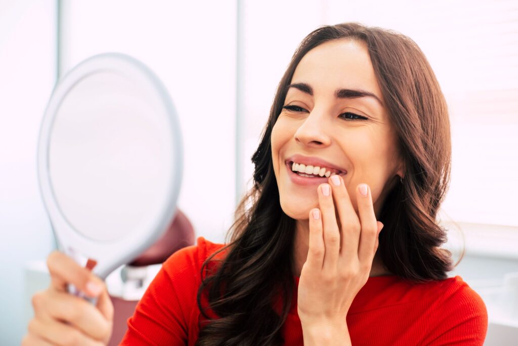 Woman in red-orange shirt touching teeth smiling at mirror